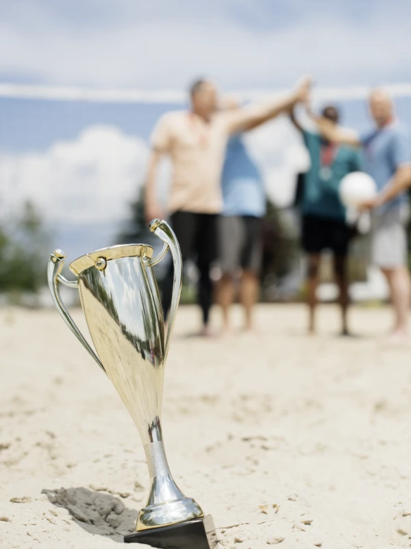 Siegerpokal im Vordergrund am Strand, im Hintergrund feiernde Gäste – besondere Momente, Events und Erlebnisse in exklusiver Atmosphäre der Villa Vie.