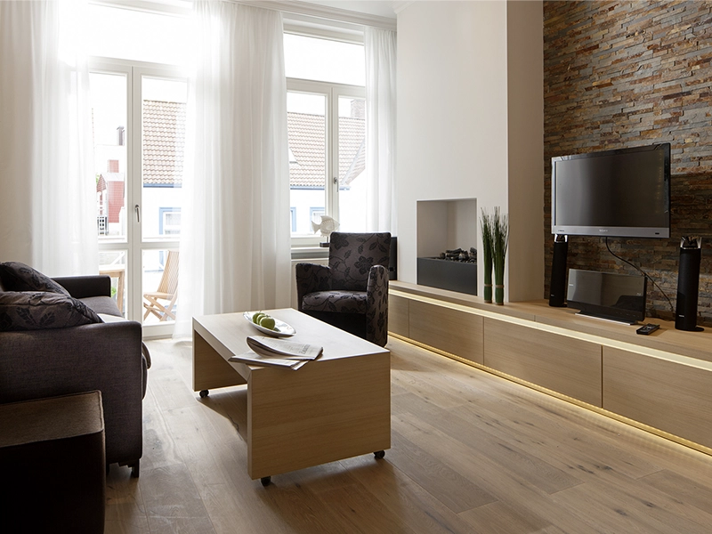 Blick in das Apartment Maison N°3 der Villa Vie auf Norderney. Zu sehen ist der Wohnbereich mit Couch, Sessel und einem TV an der Wand.