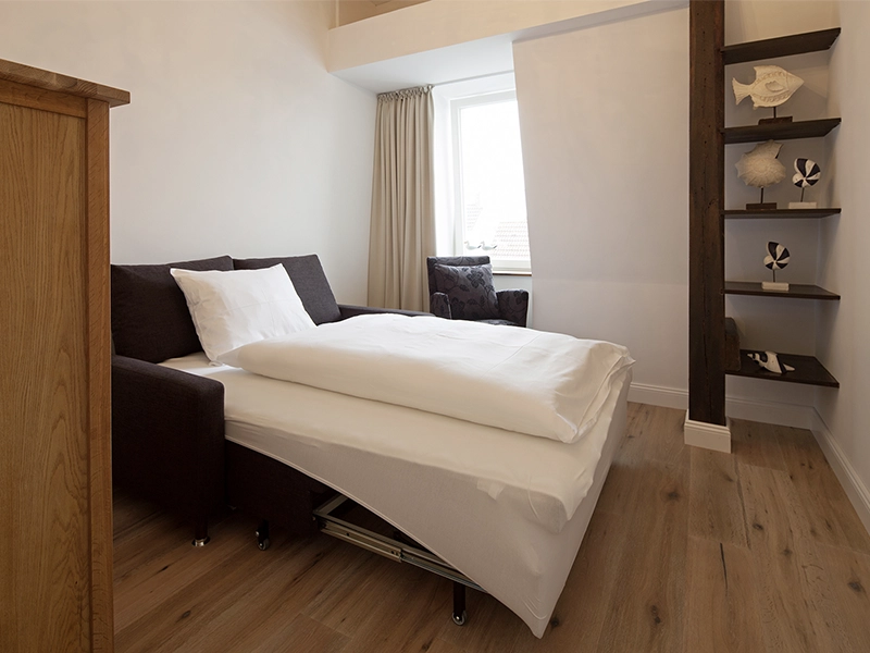 Blick in das Apartment Maison Penthouse N° 5 der Villa Vie auf Norderney. Zu sehen ist ein Schlafzimmer mit ausziehbarer Schlafcouch.