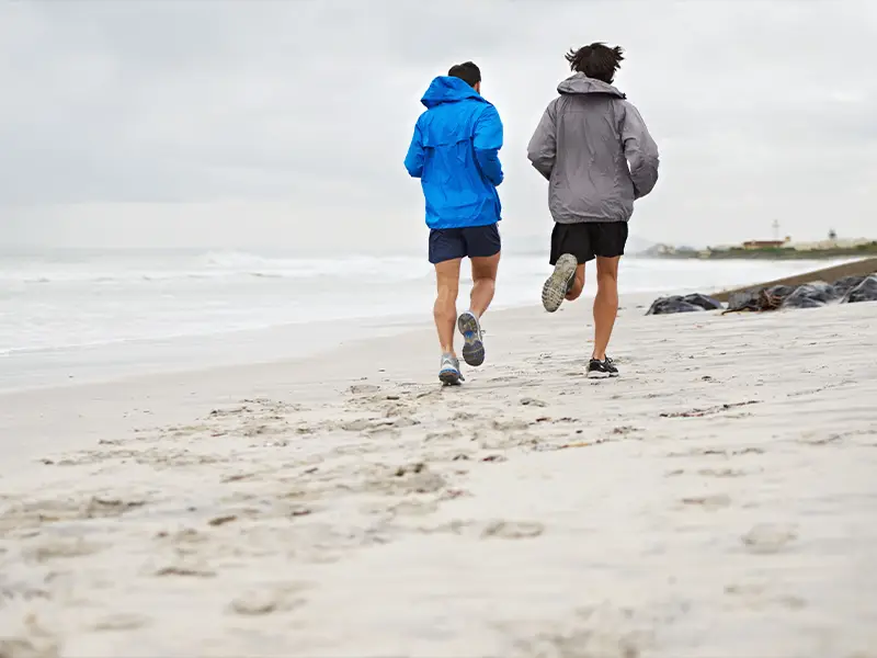 Zu sehen sind zwei junge Männer, die am Strand der Norderney entlang joggen.