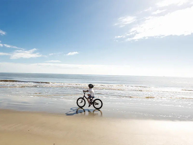 Zu sehen ist ein kleines Kind, welches bei strahlendem Sonnenschein am Strand der Norderney Fahrrad fährt.