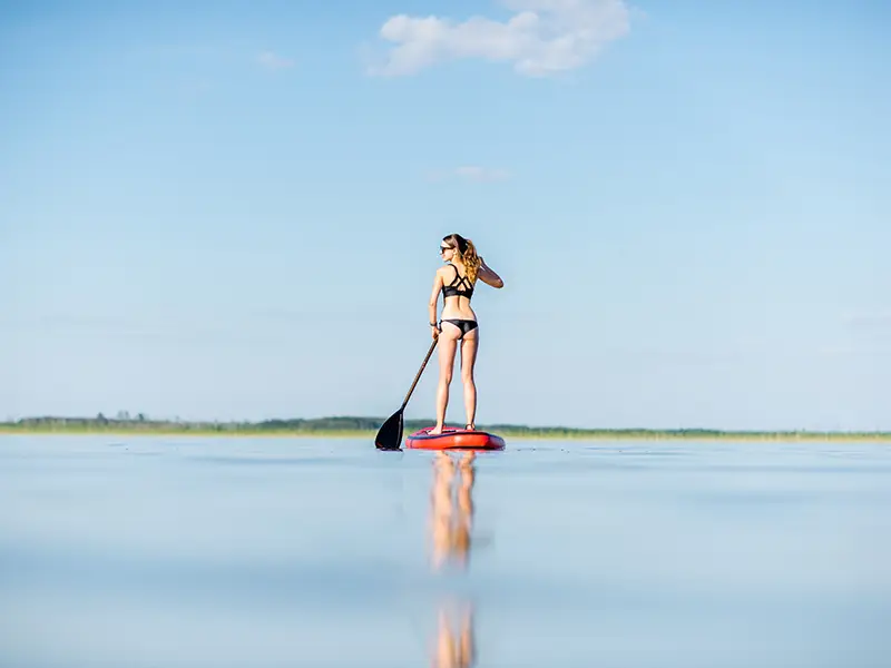 Zu sehen ist eine jungen Frau, die beim Stand Up Paddling auf der Norderney das gute Wetter genießt.