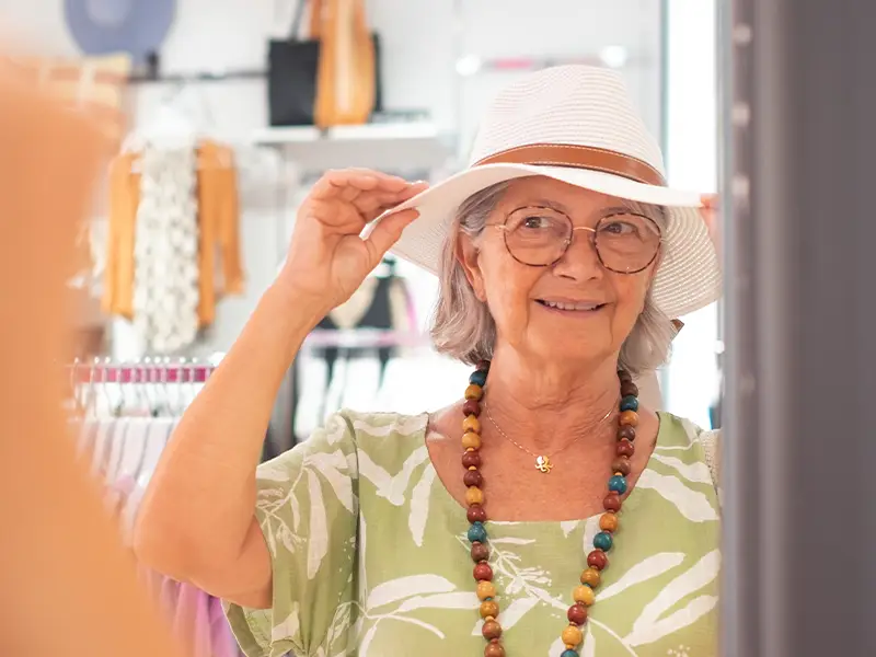 Zu sehen ist eine ältere Dame, die glücklich ihren neuen Hut anprobiert in einem Shop auf Norderney.