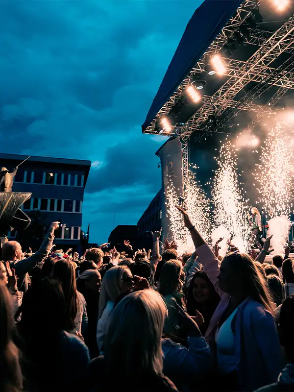 Ein feiernde Menschenmenge vor einer Musikbühne, Feuerwerk geht in die Luft und alle feiern ausgelassen.