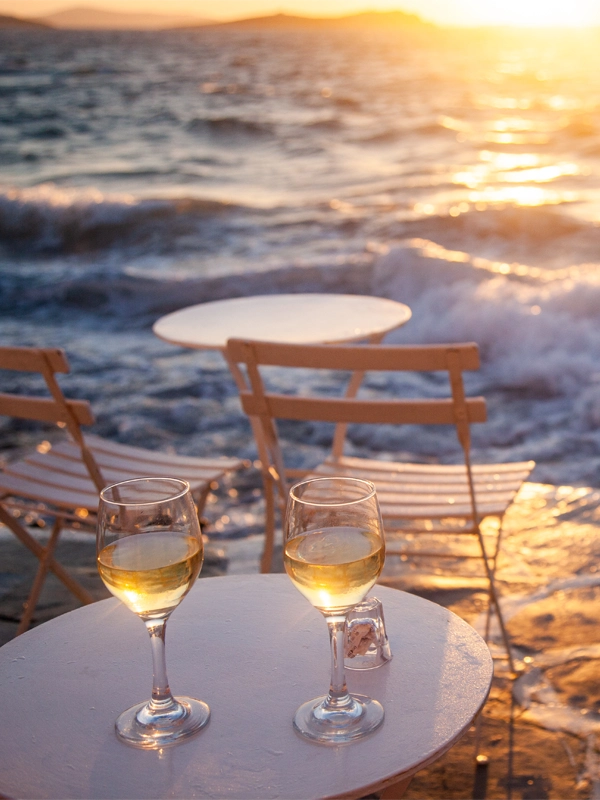 Zwei Gläser Weißwein auf einer Terrasse direkt am Meer bei Sonnenuntergang – entspannte Urlaubsatmosphäre und exklusiver Genuss in der Villa Vie.