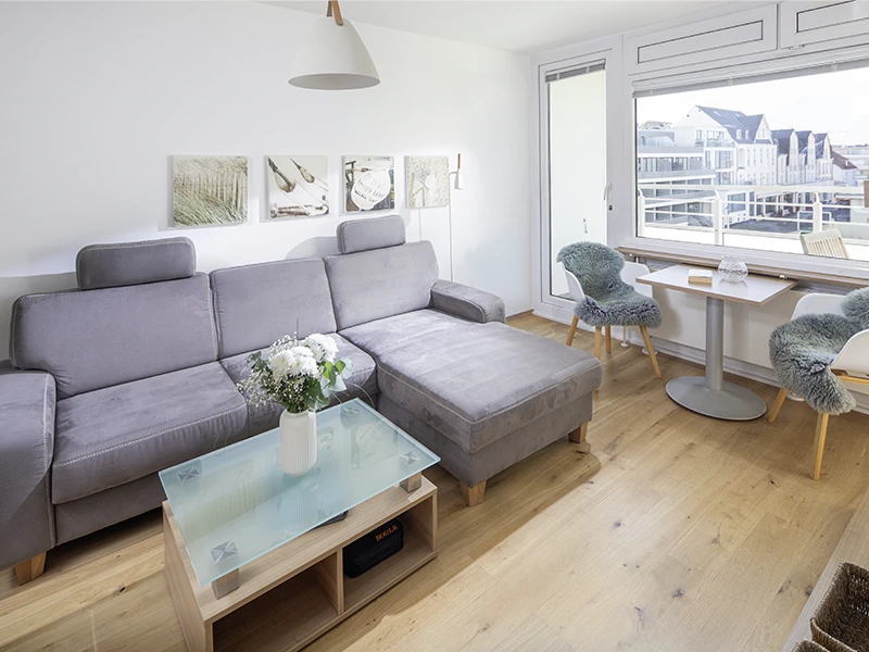 Heller Wohnbereich im Apartment Nordseeblick mit grauem Sofa, Couchtisch und Sitzplatz am Fenster