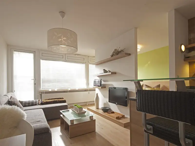 Das Apartment Nordseeblick der Villa Vie auf Norderney. Auf dem Bild sieht man den Wohnbereich, inkl. TV und mit Küchenanschnitt