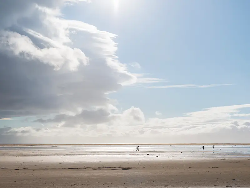 Zu sehen ist ein ruhiger Strand mit hellem Himmeln und wenig Wolken.